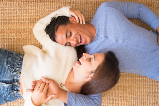 Happy young couple have fun together laying on the carpet floor at home and looking each other with smile and laugh. Cheerful man and woman in relationship enjoy life and day
