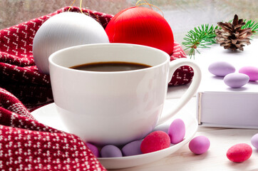 Cozy concept. Cup of coffee with colorful sweets, christmas toys and a warm scarf on a wooden windowsill