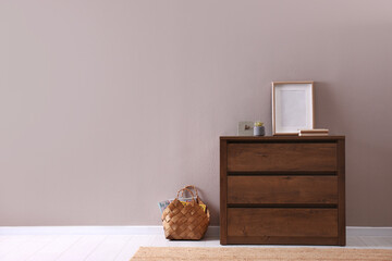 Wooden chest of drawers with decor and empty frame near light wall in room, space for text. Interior design