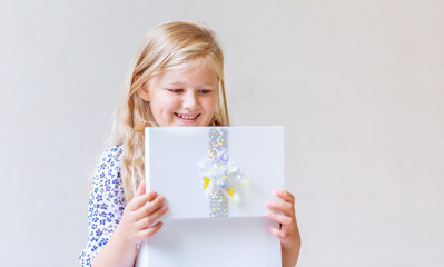 A little girl smiling looks into an open gift box. She is happy to receive a pleasant surprise.