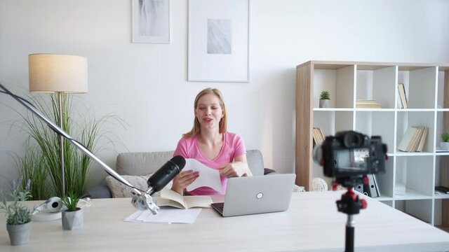 Video conference. Female tutor. Language lesson. Happy woman shooting on photo camera with paper tasks in light home studio interior.