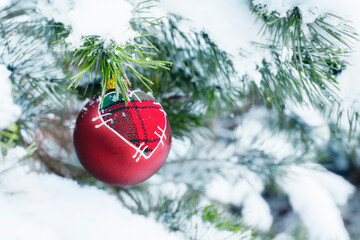 A red bauble with a heart hung on a snow-covered Christmas tree twig 
