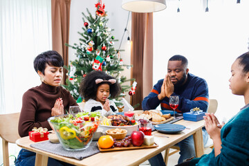 Families together to pray before meals at home. Celebration holiday togetherness near Christmas tree. African American family. Merry Christmas.