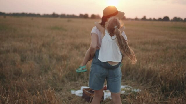 A family picnic in a wheat field and a mother with her daughter on her back whirl and laugh. Slow motion