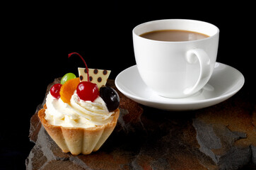 cup of coffee and delicious cake on black background