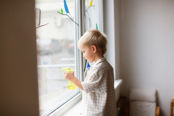 Cute boy toddler blond toddler at the window washes the glass. Helping children with household...