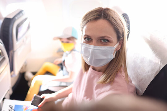 Young woman in protective mask making selfie in cabin of plane