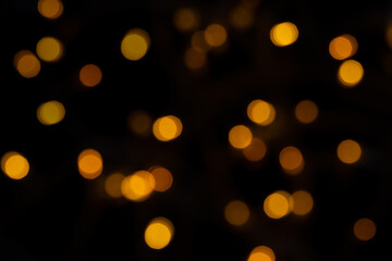 Defocused bokeh lights on black background, an abstract naturally blurred backdrop for Christmas eve or birthday party. Festive light texture. Yellow and red garland in blur. Overlay effect for design