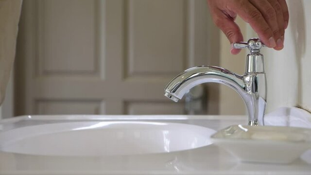 Guy turn on faucet valve, water start running to sink, slow motion shot. Camera show close view of single faucet nozzle with cold water, strong flow pouring down. Common bathroom equipment