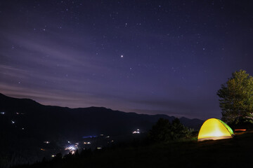 Fototapeta na wymiar Beautiful view of mountain landscape with glowing yellow camping tent at night
