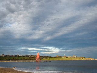 Fototapeta na wymiar The Groyne Lighthouse on Littlehaven Beach, in sunset light, blue sky, Tynemouth across River Tyne