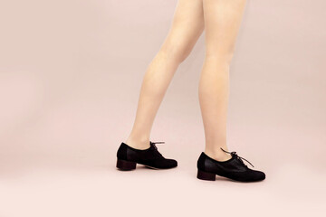 Black suede lace up shoes and woman's caucasian legs on light powdery pink background. English brogue Oxfords shoes. Studio shot photo. Copy apace.