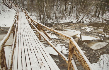 A wooden bridge with railings across the river Riezupe on a winter day. Pieces of ice in the water, Latvia.