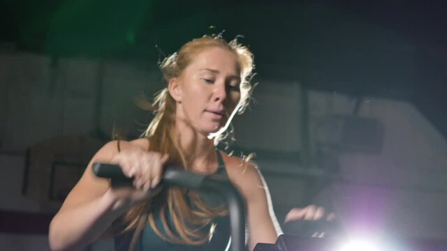 Athletic ginger-haired woman with ponytail in sportswear works out actively training muscles and strength in large sports room closeup