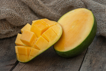 Beautiful two pieces of ripe yellow mango on a wooden textured table, one of them is cut into cubes
