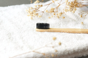Natural bamboo toothbrush on white towel with flowers on background.
