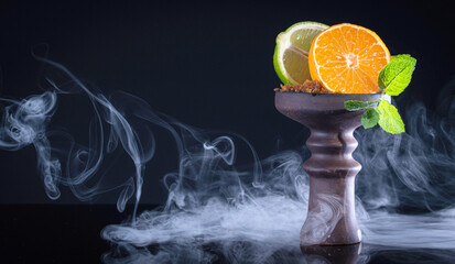 fruit hookah bowl with tobacco, tangerine, lime, mint and smoke on black background