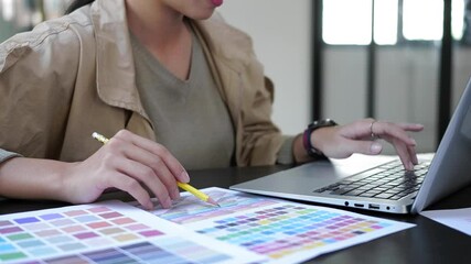 Graphic designer pointing on color swatch and typing on keyboard of laptop computer.