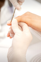 Close up of manicure master with manicure scissors removes cuticles on female nails at a beauty salon