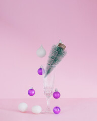 Christmas baubles coming down.Christmas tree in champagne glass.Ornaments vivid violet and snowy white on a pink background.New Year holidays concept