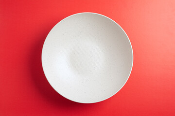 Top down minimalist view of a white bowl on yellow background. White round plate on red background