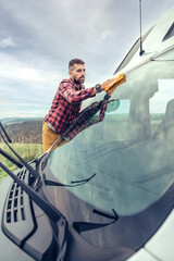 Young man cleaning camper van windshield with cloth outdoor