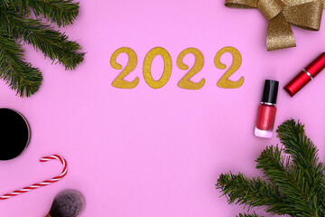 Happy New Year 2022. Golden numbers, fir branches and cosmetics on a pink background. the concept...