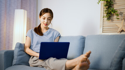 ソファーでノートパソコンを使う若い女性