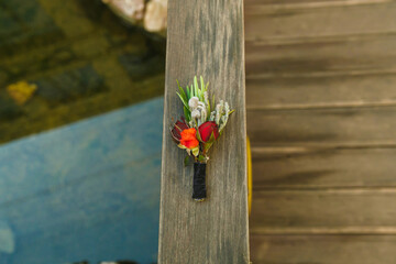 boutonniere of roses and pine needles lying on a wooden balcony railing