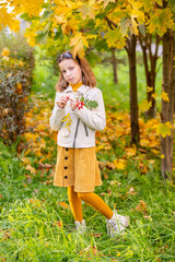 Teens fashion. Portrait of a young brunette girl in beige leather jacket in the background of autumn park.cute girl in yellow skirt stands near red rowanberry tree