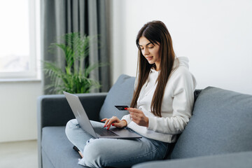 Obraz premium Young pretty woman working with laptop and credit card at home