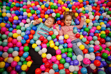 Fototapeta na wymiar Brother with sister playing in colorful ball pit. Day care indoor playground. Balls pool for children. Kindergarten or preschool play room.