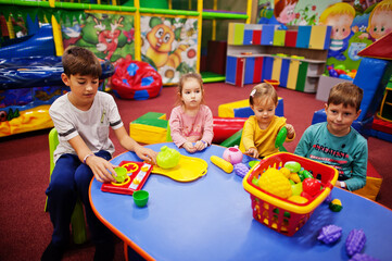 Four kids  playing in indoor play center. Kindergarten or preschool play room. Sitting by the table with plastic fruits.