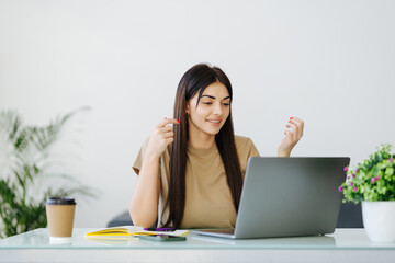 Surprised woman looking computer screen indoor. Excited girl chatting on laptop computer. Happy businesswoman closing face in front of notebook in home office.