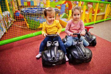 Obraz na płótnie Canvas Two siters rides on a plastic cars in indoor play center.