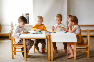group of four cute children of preschool children at the table draw on paper with multicolored...