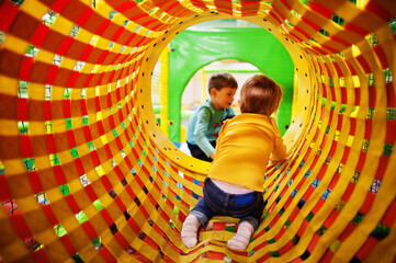 Kids playing in indoor play center. Kindergarten or preschool play room.  Baby girl climbs into the pipe.