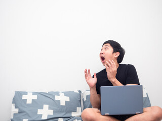 Man with laptop sitting on the bed feeling amazed looking at copy space