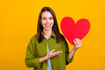 Photo of charming shiny young woman dressed green shirt smiling pointing arm big red heart isolated...