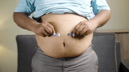 Unrecognizable unhealthy obese man checking stomach or waist fat using measuring tape before diet at home - concept of suffering body overweight due to junk food habits