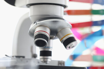Fototapeta na wymiar Microscope standing near multicolored model of dna chain in lab