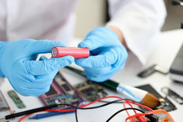Master holding electronic battery near microchips in workshop closeup