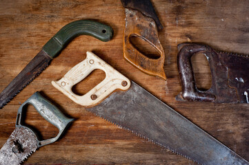 Old vintage metal saws for wood of different shapes and sizes, crumpled on a wooden background.