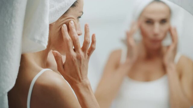 Beautiful Caucasian Woman Touches Her Perfect Soft Shoulder, Neck, Sensually Looks in Bathroom Mirror. Middle Aged Female Enjoying Her Natural Beauty Morning Routine. Artistic Gradual Focusing