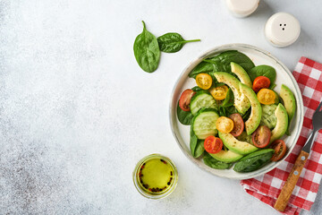 Avocado, red, yellow, black cherry tomato, spinach and cucumber fresh salad with spices pepper and olive oil in grey bowl on grey slate, stone or concrete background. Healthy food concept. Top view.