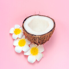 Half of coconut, plumeria flowers on pink background. Spa concept.