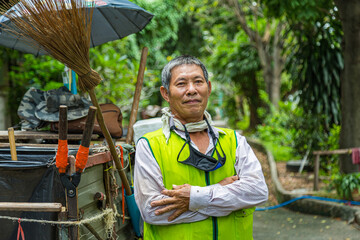 Portrait happy old Asian man street cleaner standing next to an old gabage cart before going to...