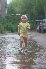 Baby girl walks in the rain through puddles in summer