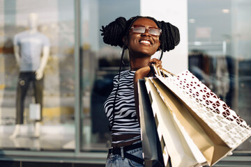 Stylish African woman with shopping bags walking down the street on a sunny day after Good Shopping on Black Friday