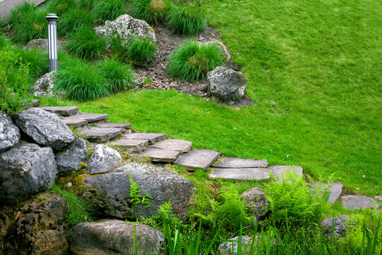 stone staircase with steps made of wild natural stone on slope of hill park landscape with rock, ground garden lantern among green plants in summer environment for eco travel, nobody.